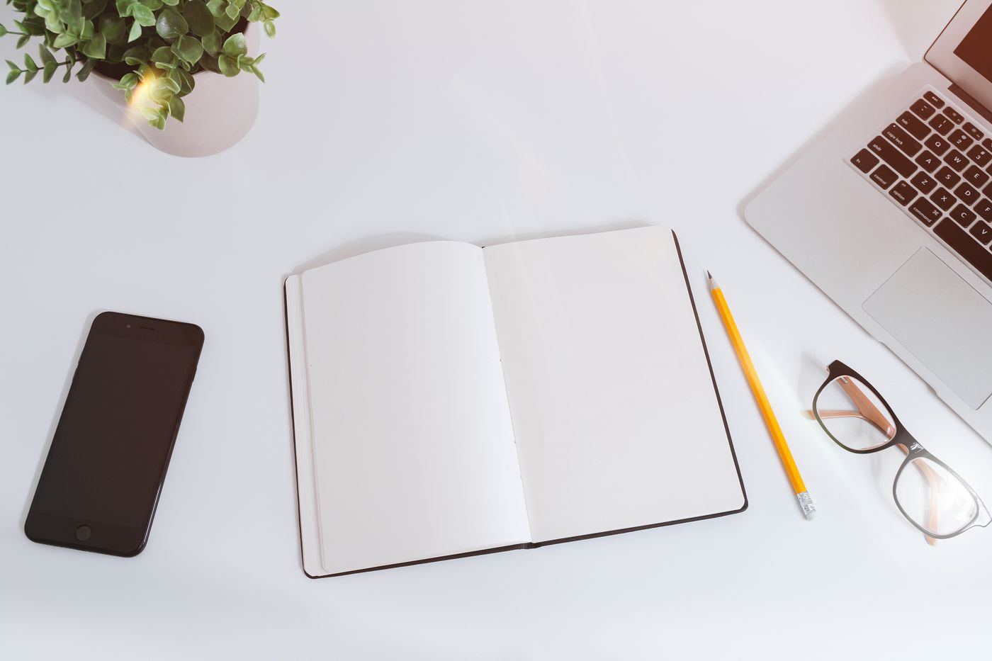 Světlý pracovní stůl s notebookem, zápisníkem, tužkou a brýlemi